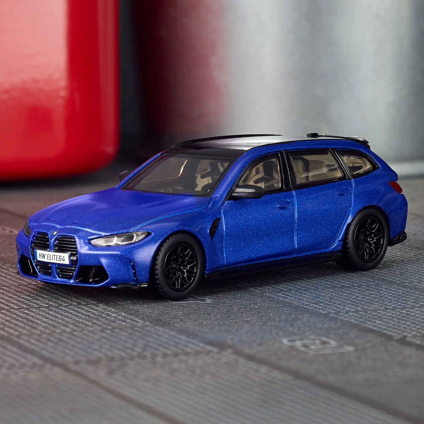 Blue model car on a metallic surface with a blurred red object in the background